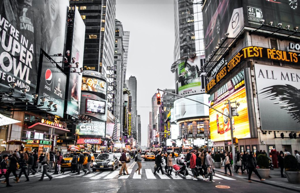pedestrians walking crosswalk in Times Square in front of large billboard ads